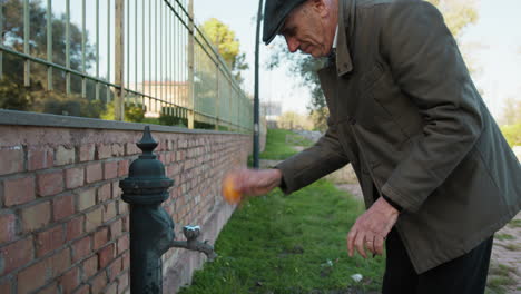 man washes a tangerine at the park fountain before eating