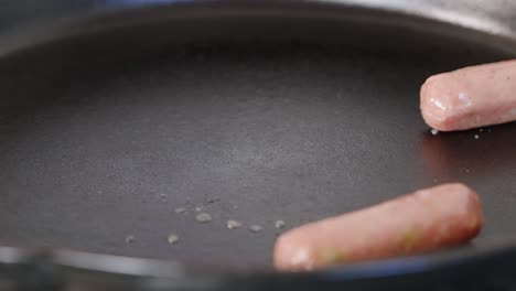 Frozen-sausage-links-dropping-into-hot-pan-and-sizzling-for-breakfast-meal-close-up-slow-motion-4k