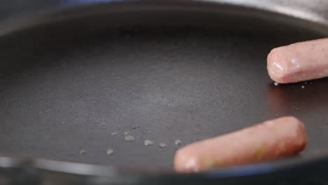 frozen sausage links dropping into hot pan and sizzling for breakfast meal close up slow motion 4k