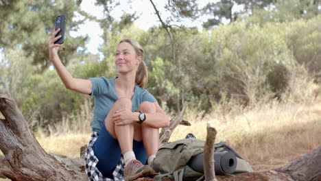 una joven mujer caucásica sonríe mientras mira su teléfono inteligente al aire libre