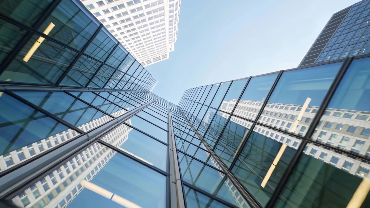 Câmera inclinando-se para cima em direção à fachada de vidro de uma torre ao nível da rua, revelando montantes e reflexos.