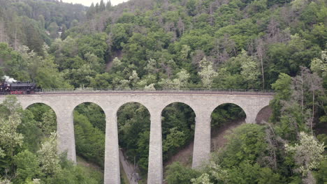 train with a steam locomotive driving over a stone viaduct in a valley