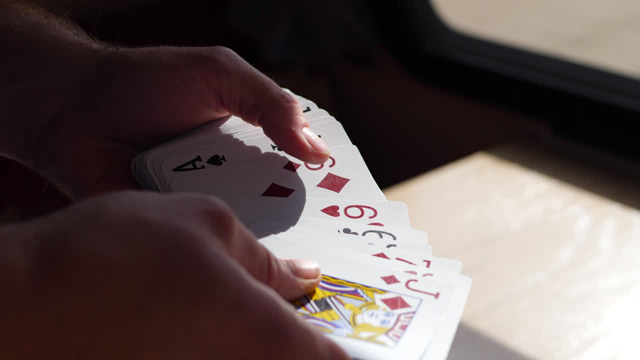 Close up on hands in slow motion rifling and shuffling through a pack of playing cards in sunlight