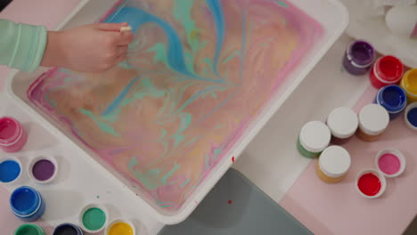 un niño pequeño dibuja una flor en la superficie del agua aceitosa con pinturas