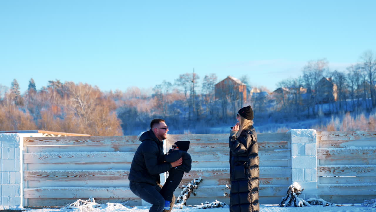 Happy mom and dad play with their baby outdoors in winter. Father tosses his son up entertaining him.