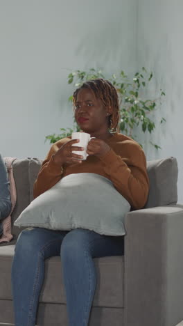 dissatisfied indian and african american women friends change channels with remote control sitting on sofa. best female companions watch tv together at home