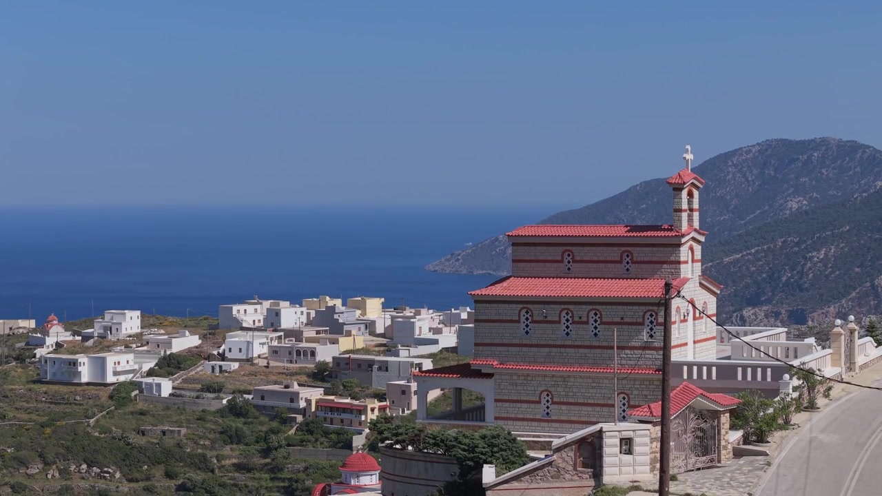 Il drone si eleva e rivela la chiesa del villaggio di Spoa, con il paesaggio aspro di Karpathos che si dispiega dietro di essa