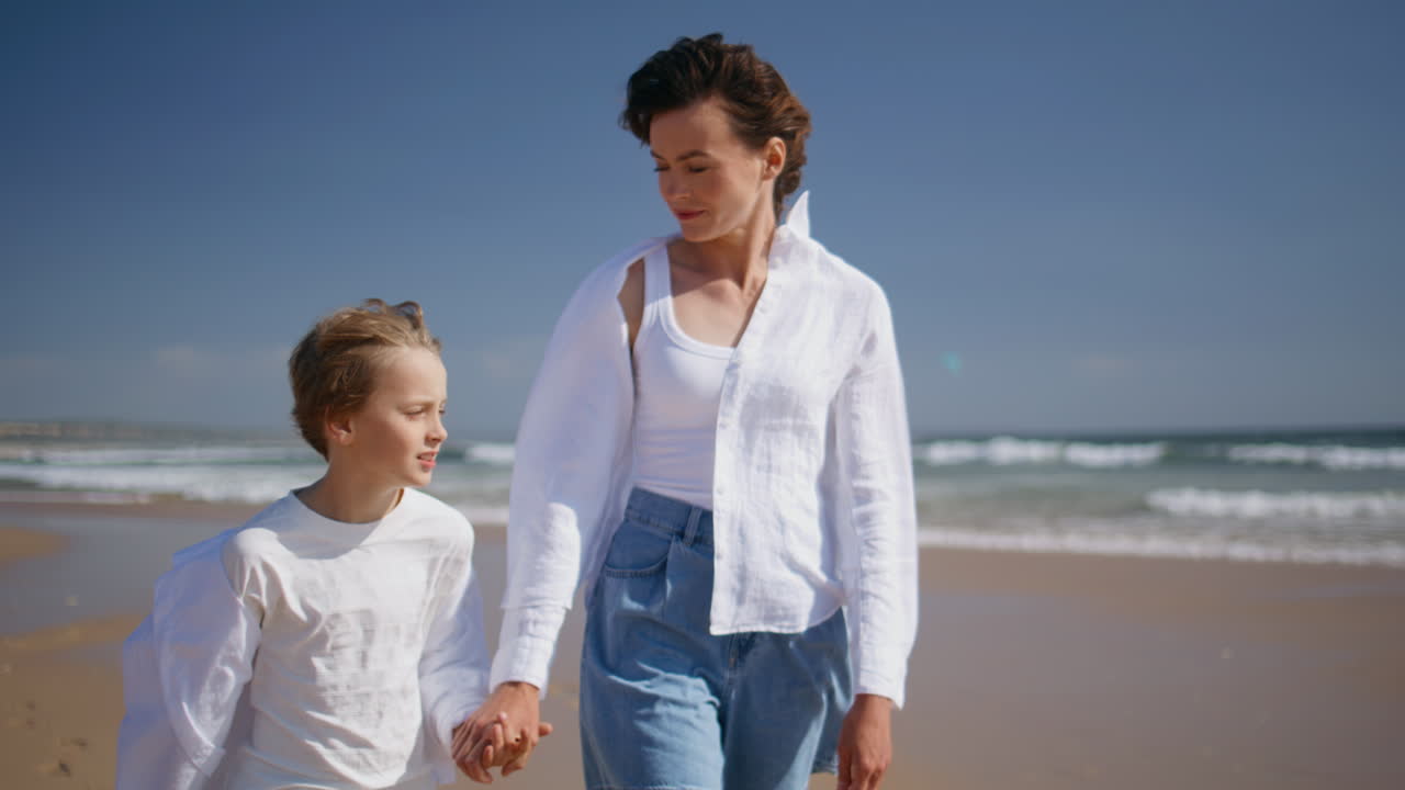 Entspannter Junge, der mit seiner Mutter an einem sonnigen, windigen Strand spaziert. Glückliche Mutter und Sohn genießen den Urlaub