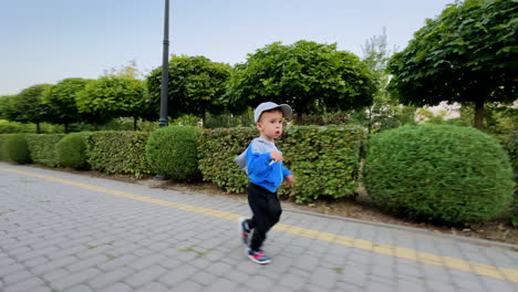 active toddler wearing sports suit and cap runs in the park. baby boy having good time outdoors.