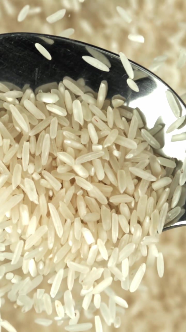Primo piano al rallentatore di chicchi di riso bianco che cadono su un cucchiaio