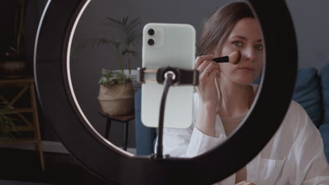 young cute vlogger woman makes a video tutorial applying make up powders with a brush on her face