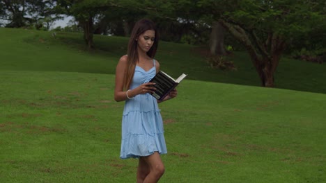 a young girl opens a book while walking on a golf course on the tropical island of trinidad