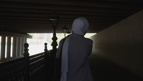 muslim woman in grey coat walks along empty embankment