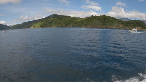 Weitwinkelansicht-Eines-Kleinen-Schnellboots,-Das-Im-Sommer-An-Größeren-Booten-Auf-Wunderschönem-Blauem-Wasser-Vorbeifährt---Strebe-Inlet,-Marlborough-Sounds