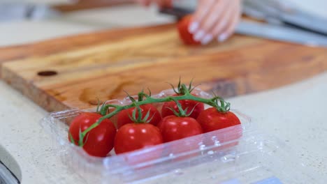 hands selecting tomatoes from a container onto a wooden cutting board in a bright kitchen setting