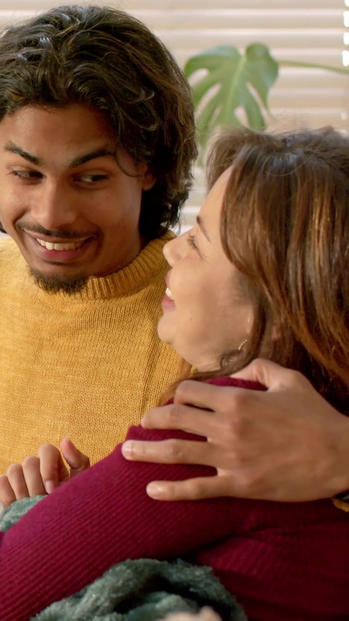 Video verticale: Uomo con maglione color senape appoggiato, tira una donna in bordeaux sul divano con una coperta verde.