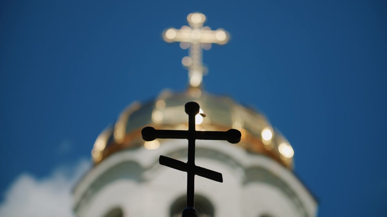 Foreground silhouette of a Christian cross with a softly blurred church dome and golden cross in the background