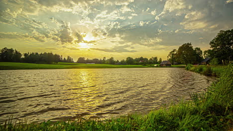 Zeitrafferaufnahme-Des-Sonnenuntergangs-über-Einer-Ländlichen-Landschaft-Mit-Häusern-An-Einem-See-Am-Abend