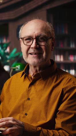 vertical video old person with spectacles enjoys reading a book at the library