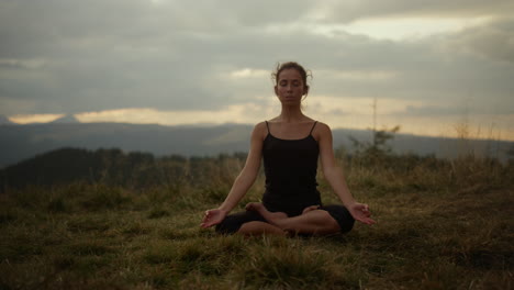 Woman-meditating-in-mountains-at-sunset.-Girl-sitting-in-lotus-pose-on-ground