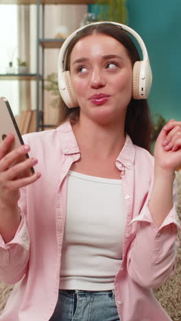 Young woman dancing on sofa wearing headphones moving arms to music smiling with joyful free energy