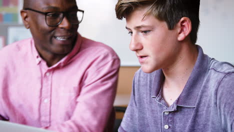 high school tutor giving male student using laptop one to one tuition at desk