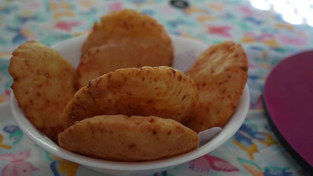 Arepa de huevo dorata disposta in una ciotola bianca, catturata in un primo piano su una tovaglia chiara e a motivi. La luce naturale soffusa evidenzia la consistenza croccante, ideale per concetti culinari