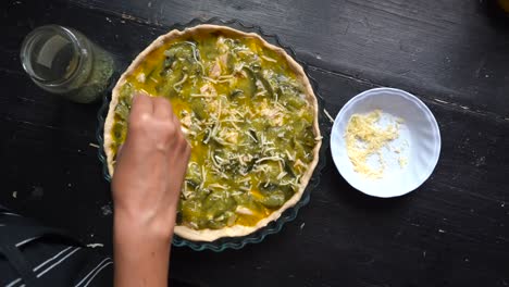 Woman's-Hand-Sprinkling-Grated-Cheese-On-Top-Of-Zucchini-Pie-Before-Baking