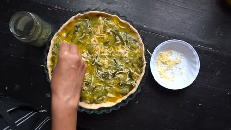 mano de mujer rociando queso rallado encima del pastel de calabacín antes de hornear