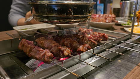 built-in chargrill table with auto turning skewers, lamb meat bbq is being cooked by visitors of korean restaurant - close-up