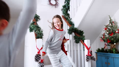 Two-Excited-Children-Wearing-Pajamas-Running-Down-Stairs-Holding-Stockings-On-Christmas-Morning