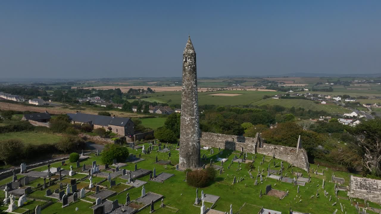St. Declan's Monastery, Ardmore, County Waterford, Ireland, September 2024. Drone pushes towards the Round Tower and 12th century graveyard with panoramic rural countryside stretching to the horizon.