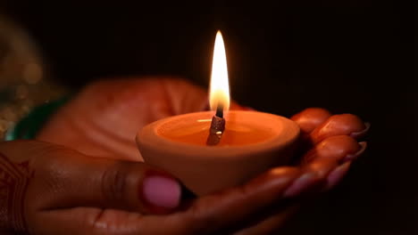hands holding a lit traditional diya (oil lamp) in darkness