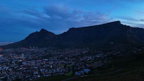 cinematic aerial view of table mountain in cape town, south africa, dramatic rocky cliffs with coastal cityscape at sunset, clouds rolling over peaks and golden evening light