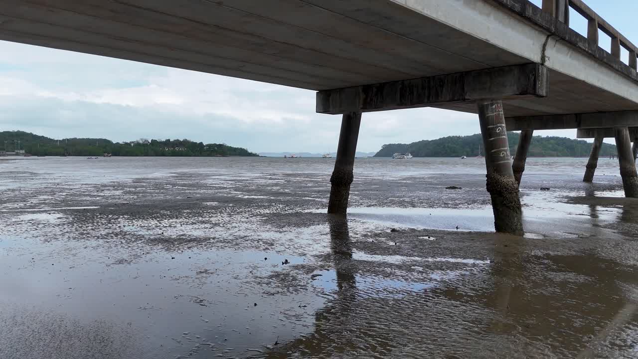 Aerial footage of a pier in Phuket, Thailand, showcasing serene coastal scenery with gentle waves and overcast skies