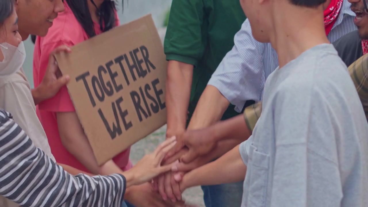 Group of diverse activists stacking hands together in gesture unity, solidarity, and commitment