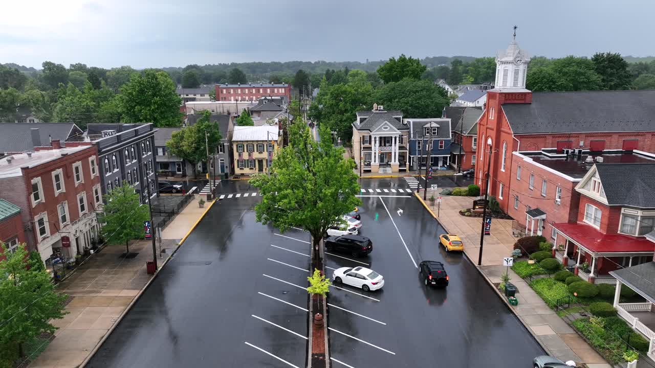 Rainy center square of american town in USA. Church with historic buildings and main street of City. Parking cars on street. Aerial rising wide shot at thunderstorm.