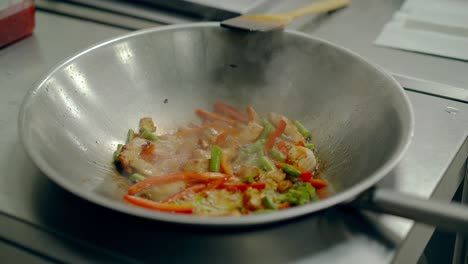 cook roasts fresh vegetables with shrimps in a frying pan stirs them