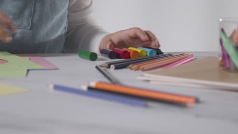 close up studio shot of young girl at table drawing and colouring in picture 1