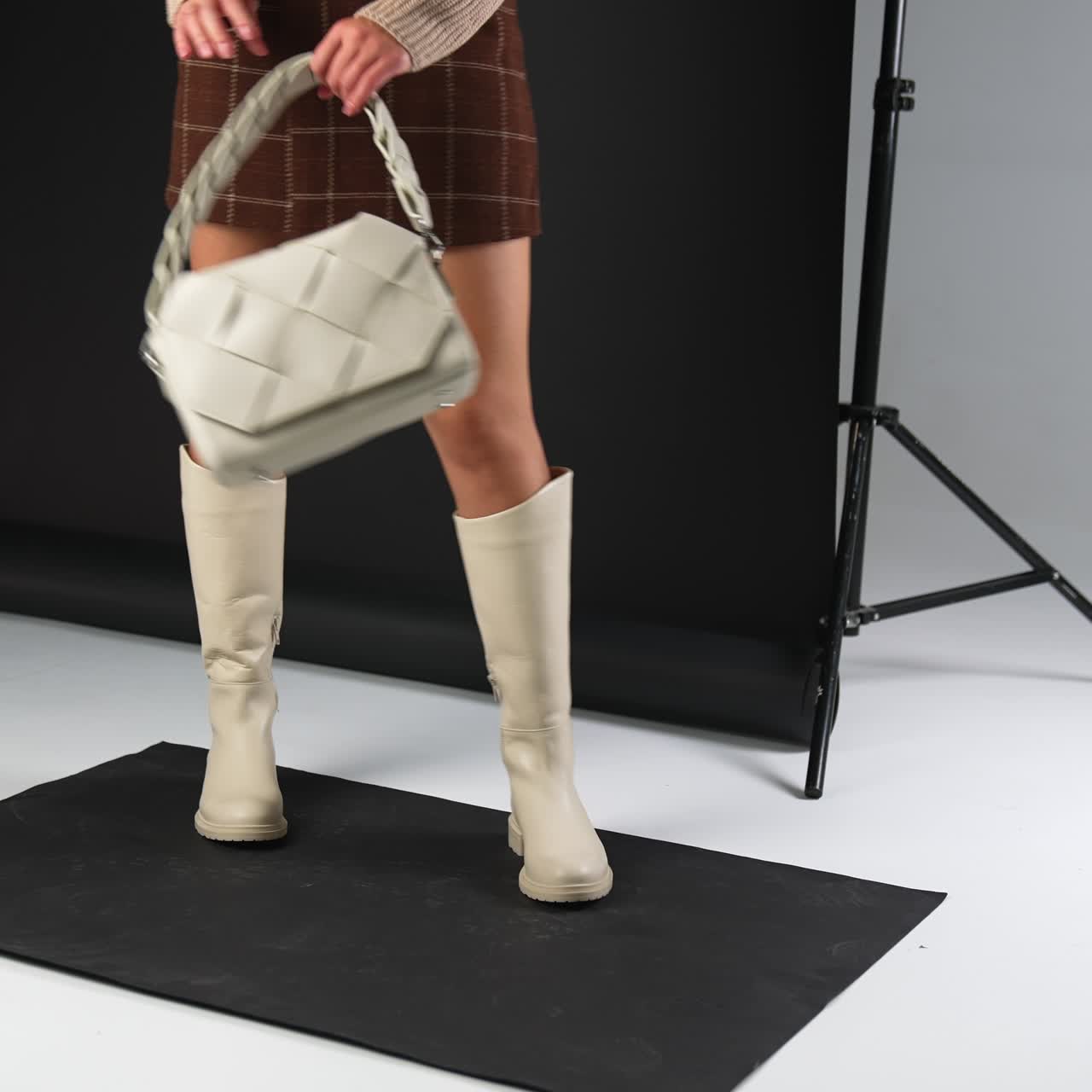 Model turns demonstrating white high boots and bag. Studio photo shoot of stylish footwear and accessories