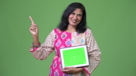 mature happy beautiful indian woman showing digital tablet and pointing finger up
