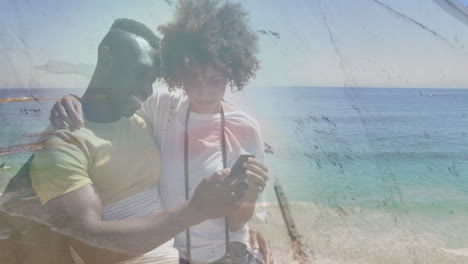 animación de una feliz pareja afroamericana usando un teléfono inteligente en la playa sobre el mar