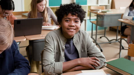 young boy smiling at his desk in a classroom