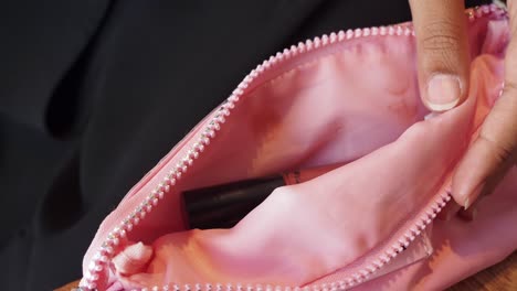 woman applying lipstick from a pink cosmetic bag