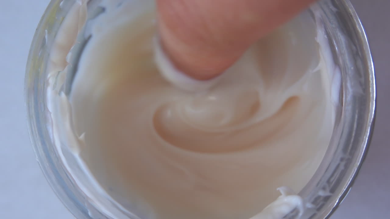 Woman finger picking up cream from a jar