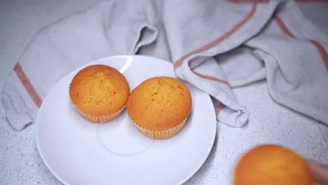 mano femenina coloca 3 pastelitos en un plato pequeño junto a un paño de cocina