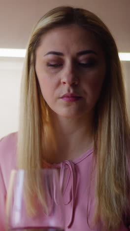 upset woman in pink dress looks at glass with expensive red wine suspecting poisoning at festive dinner in modern kitchen at home slow motion