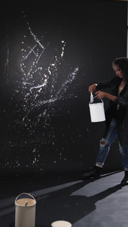vertical video: artist in leather jacket creating abstract splatter art on dark wall