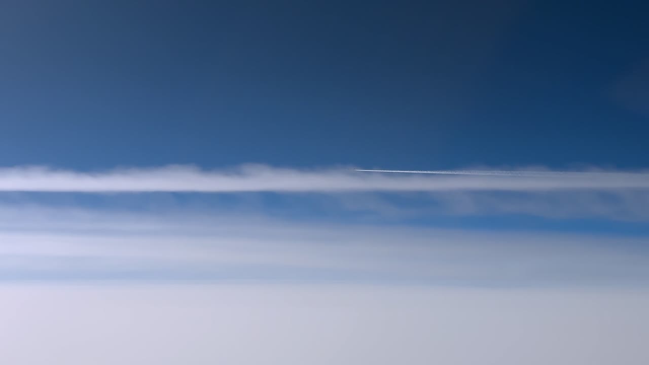 青空の中、層積雲の層の上を以前のジェット機の飛行機雲に乗って飛行するジェット機の空撮右側面からの眺め。