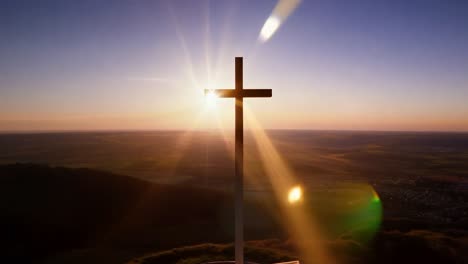 sunrise illuminates a cross atop a mountain, creating a beautiful lens flare against the vibrant sky